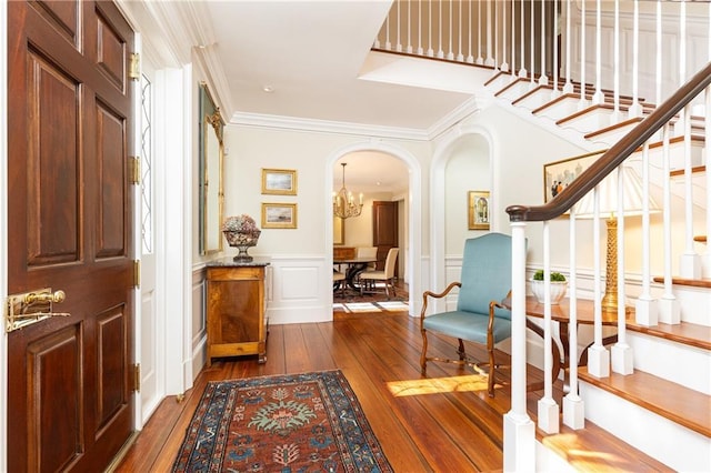 foyer with ornamental molding, dark wood finished floors, arched walkways, wainscoting, and a decorative wall