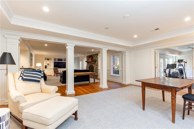 interior space with visible vents, ornamental molding, wood finished floors, a fireplace, and decorative columns