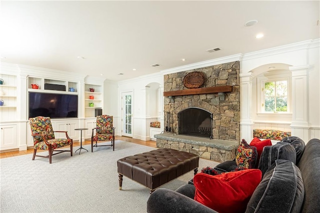 living room featuring wood finished floors, visible vents, ornate columns, a stone fireplace, and crown molding