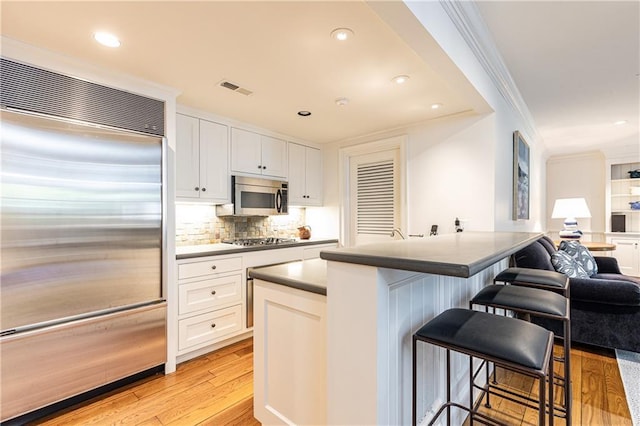 kitchen featuring crown molding, a breakfast bar area, light wood-style flooring, white cabinets, and stainless steel appliances