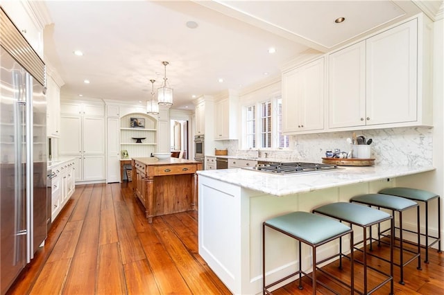 kitchen with white cabinets, a peninsula, stainless steel appliances, and wood-type flooring