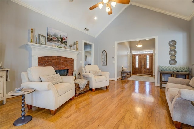 living area with ceiling fan, light wood-style floors, a brick fireplace, baseboards, and high vaulted ceiling