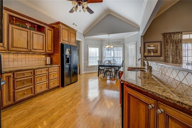 kitchen with black fridge, a sink, brown cabinetry, vaulted ceiling, and a ceiling fan