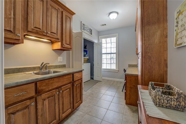 kitchen with a sink, brown cabinets, light tile patterned flooring, and baseboards