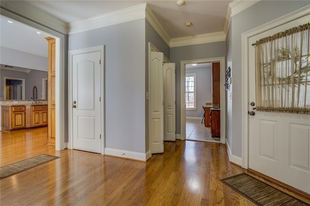 entryway with light wood finished floors, baseboards, and ornamental molding
