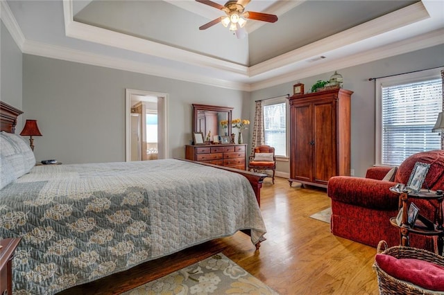 bedroom with a raised ceiling, light wood-style floors, and crown molding