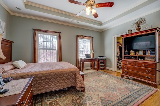 bedroom with a tray ceiling, crown molding, light wood-style floors, ceiling fan, and baseboards
