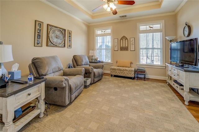 living area with ceiling fan, crown molding, a raised ceiling, baseboards, and light wood-type flooring