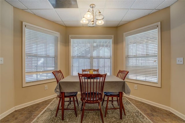 tiled dining area with a chandelier, a drop ceiling, and baseboards