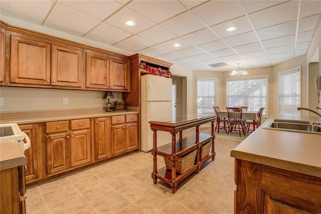 kitchen featuring freestanding refrigerator, a sink, brown cabinets, a drop ceiling, and recessed lighting