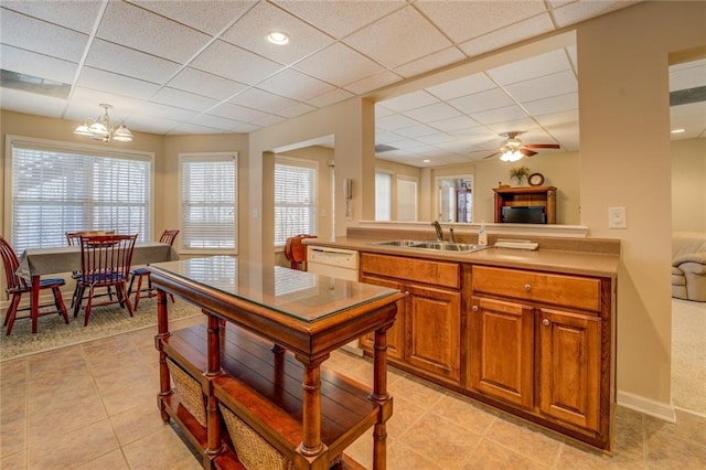 kitchen featuring a sink, a drop ceiling, plenty of natural light, white dishwasher, and light tile patterned floors