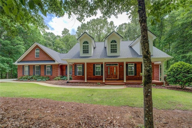 new england style home featuring brick siding, covered porch, a front yard, and roof with shingles