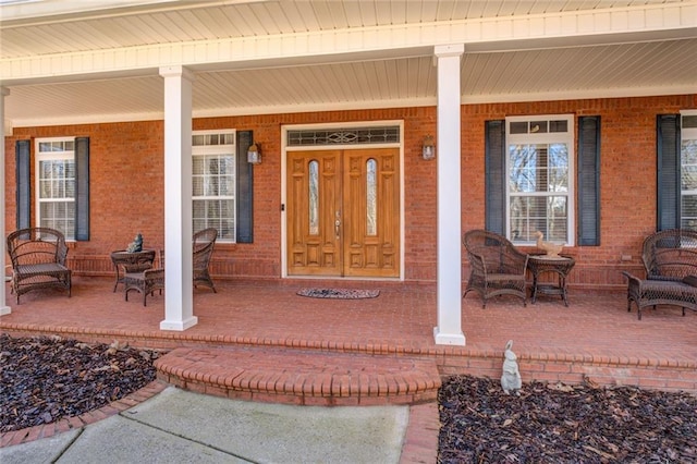 doorway to property with a porch and brick siding