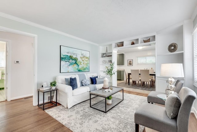 living room with light hardwood / wood-style floors, built in shelves, and ornamental molding