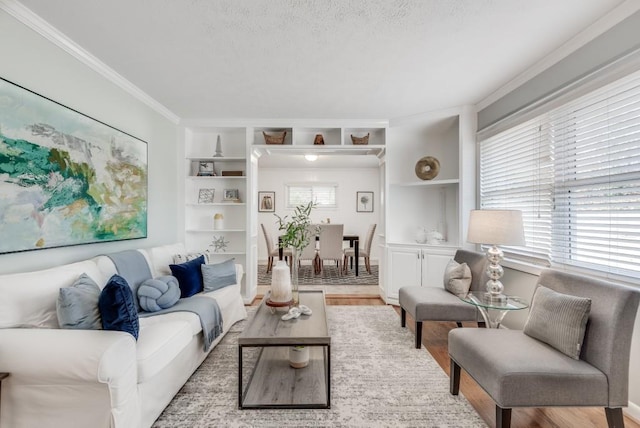 living room with light hardwood / wood-style floors, a textured ceiling, built in features, and crown molding