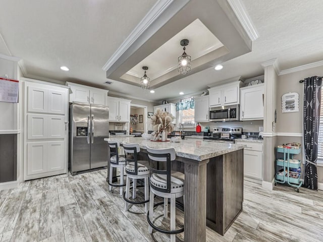 kitchen featuring ornamental molding, an island with sink, appliances with stainless steel finishes, light stone counters, and white cabinetry