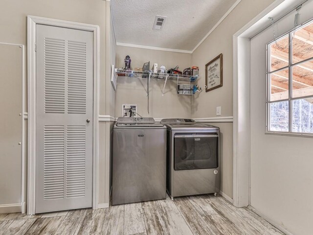 laundry room featuring a textured ceiling, separate washer and dryer, ornamental molding, and light hardwood / wood-style floors