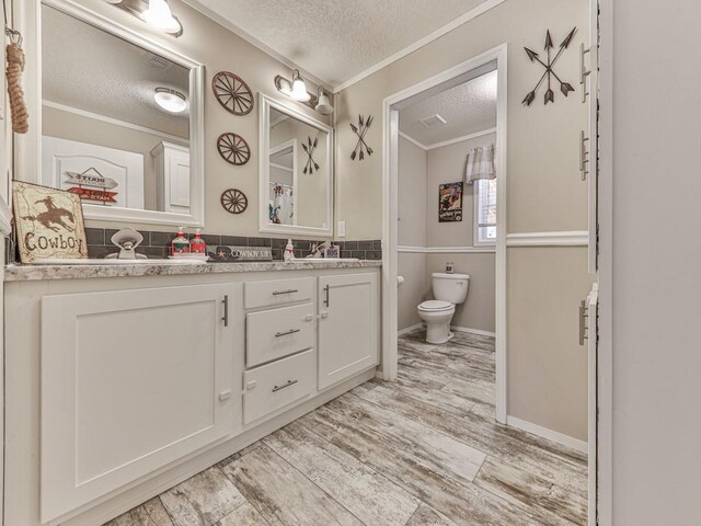 bathroom featuring wood-type flooring, a textured ceiling, toilet, vanity, and ornamental molding