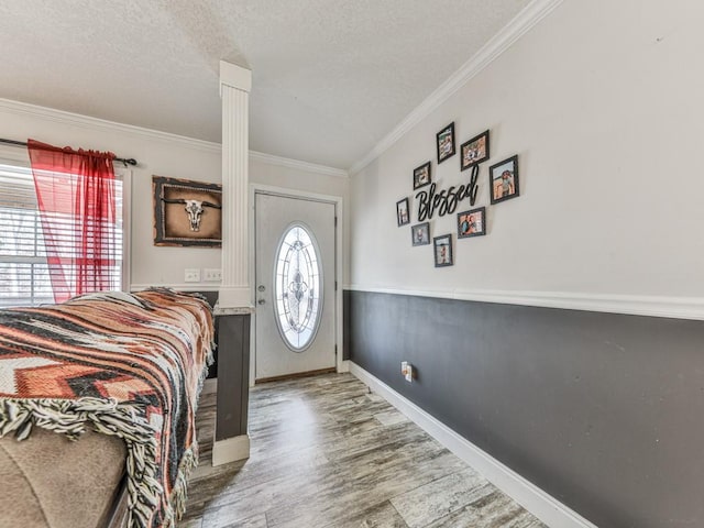 foyer with hardwood / wood-style floors, ornamental molding, a textured ceiling, and decorative columns