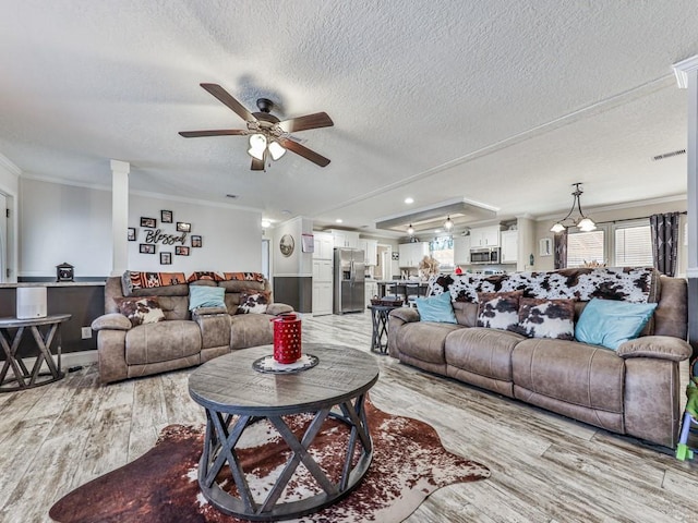 living room with a textured ceiling, ceiling fan, light wood-type flooring, and crown molding