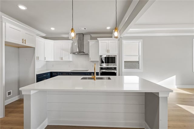 kitchen with wall chimney exhaust hood, decorative light fixtures, white cabinets, sink, and stainless steel appliances