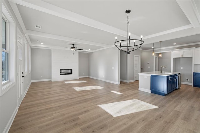 kitchen featuring blue cabinetry, white cabinetry, a large fireplace, decorative light fixtures, and a center island with sink