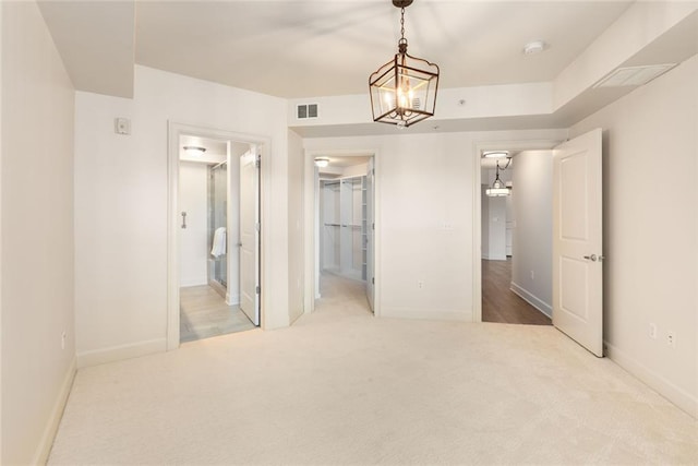unfurnished bedroom with a walk in closet, a notable chandelier, carpet flooring, and baseboards