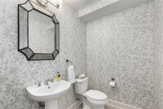 bathroom featuring baseboards, toilet, wallpapered walls, and a sink