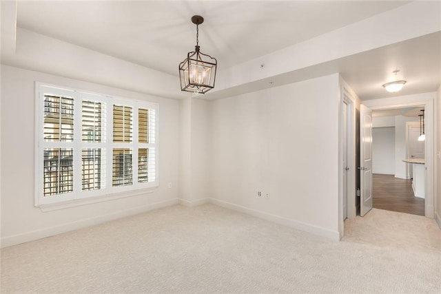 spare room featuring carpet floors, baseboards, and a chandelier