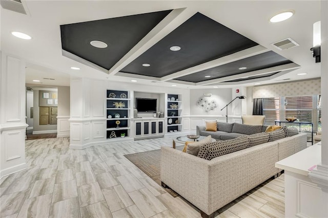 living area with coffered ceiling, visible vents, a decorative wall, and ornate columns