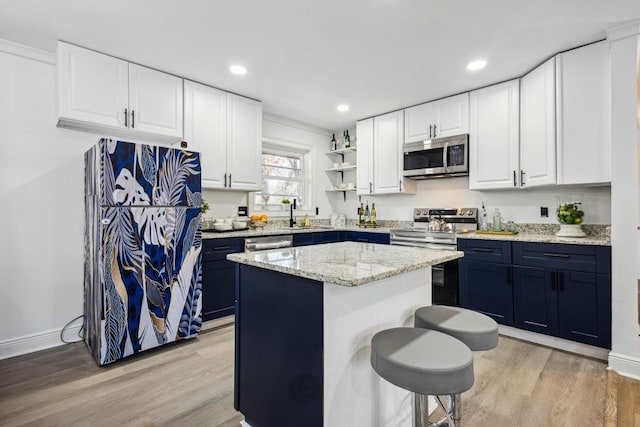 kitchen featuring a center island, light wood-type flooring, appliances with stainless steel finishes, a kitchen breakfast bar, and white cabinets