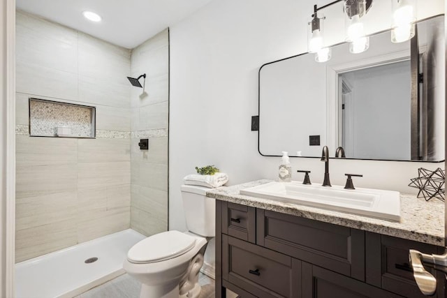 bathroom featuring toilet, a tile shower, and vanity