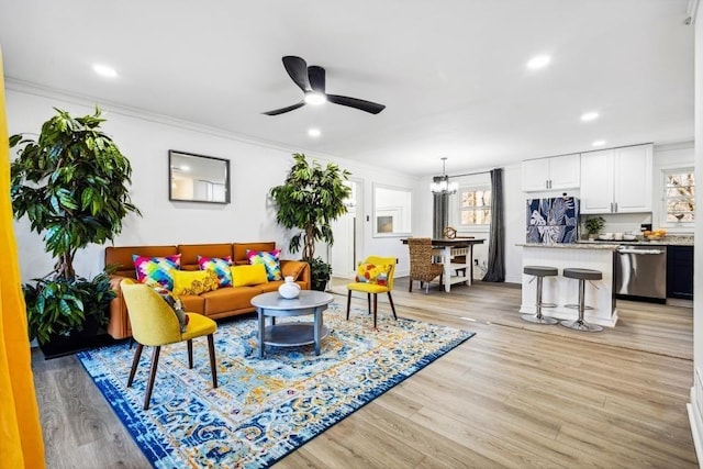 living room with crown molding, ceiling fan with notable chandelier, and light hardwood / wood-style flooring