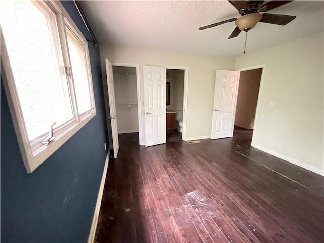 unfurnished bedroom with a walk in closet, ceiling fan, baseboards, a closet, and dark wood-style floors