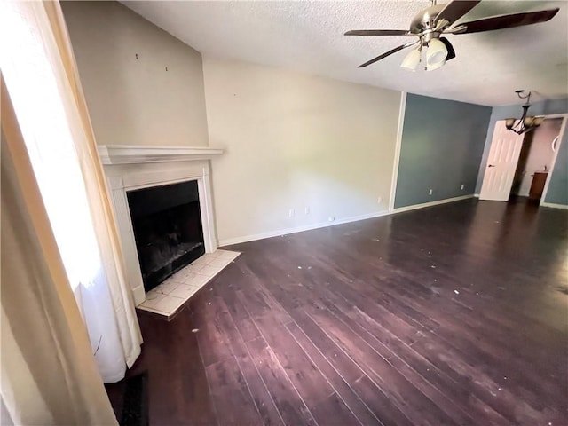 unfurnished living room featuring a ceiling fan, a textured ceiling, a tiled fireplace, wood finished floors, and baseboards