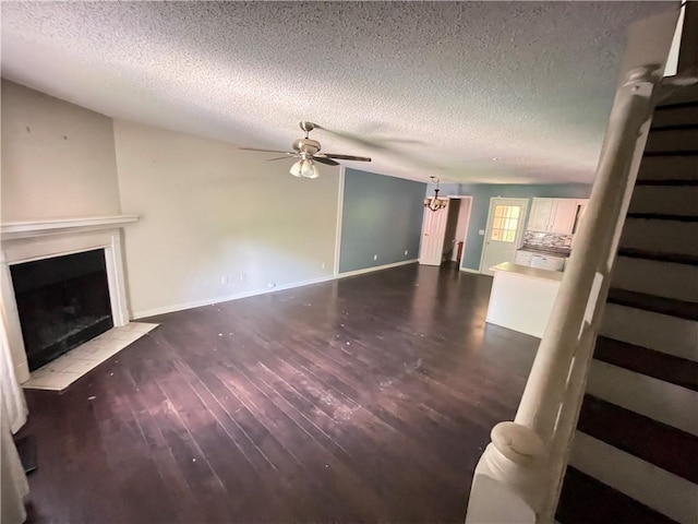 unfurnished living room featuring a textured ceiling, stairs, ceiling fan with notable chandelier, and a fireplace with flush hearth