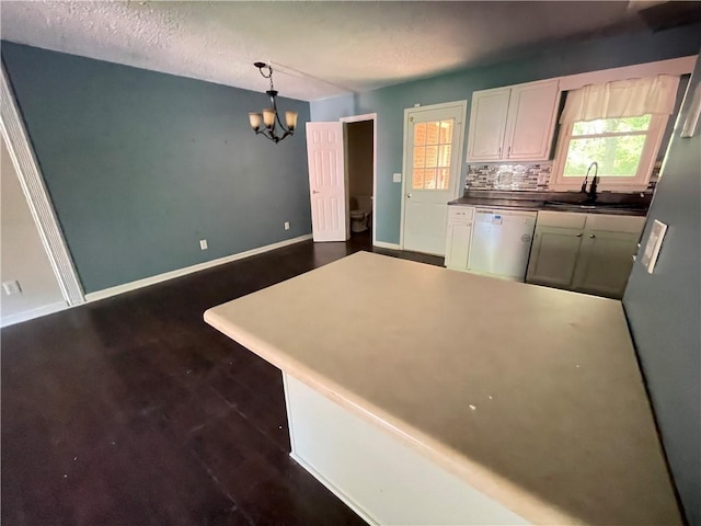 kitchen with a peninsula, white dishwasher, a sink, a notable chandelier, and decorative light fixtures