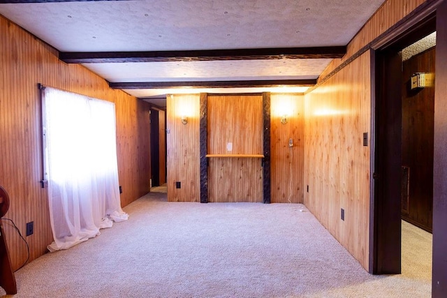 unfurnished room with beamed ceiling, light colored carpet, a textured ceiling, and wooden walls