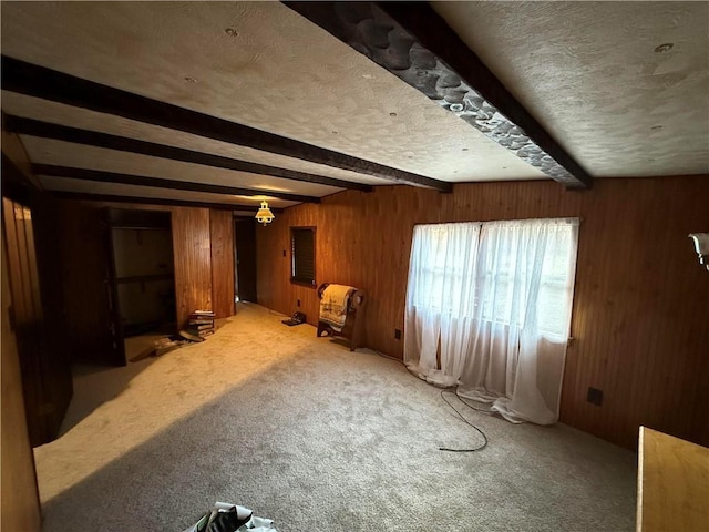 interior space featuring a textured ceiling, wooden walls, beamed ceiling, and carpet flooring