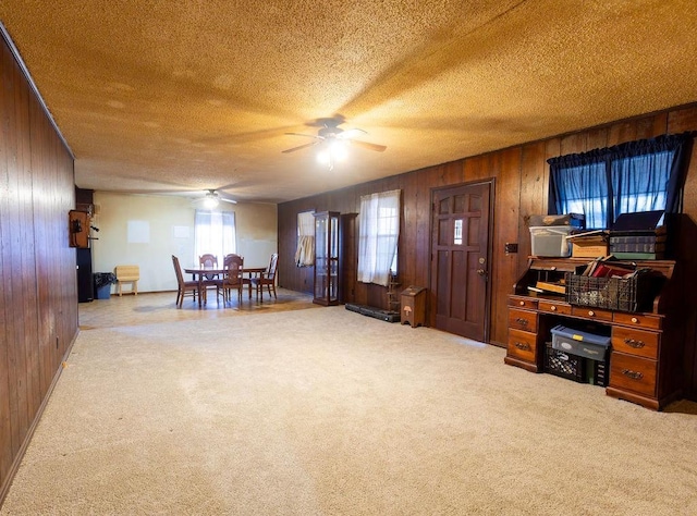 interior space featuring carpet, a textured ceiling, ceiling fan, and wood walls