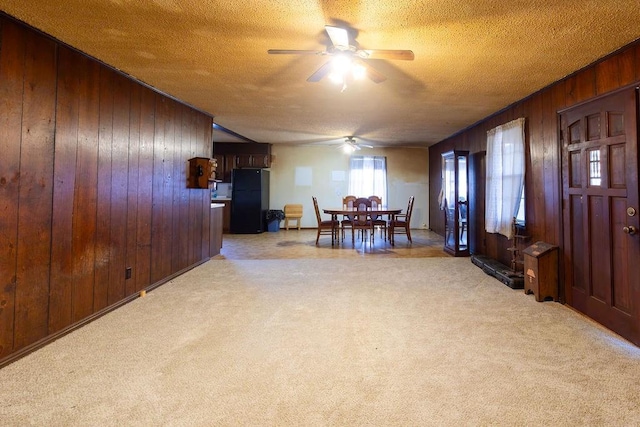 carpeted dining space featuring ceiling fan, wooden walls, and a textured ceiling