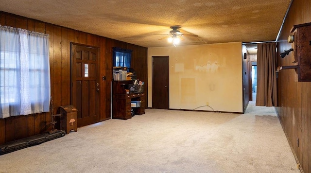 interior space featuring ceiling fan, a textured ceiling, and wood walls