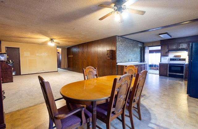 carpeted dining space with ceiling fan, a textured ceiling, and wood walls