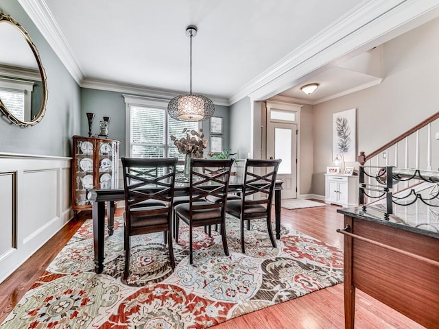dining area with wood finished floors, crown molding, stairs, wainscoting, and a decorative wall