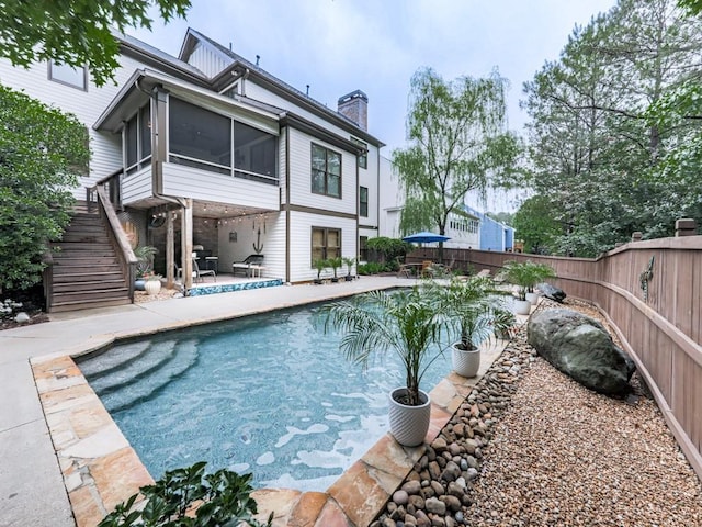 back of property featuring a fenced backyard, a patio area, a chimney, a sunroom, and stairs