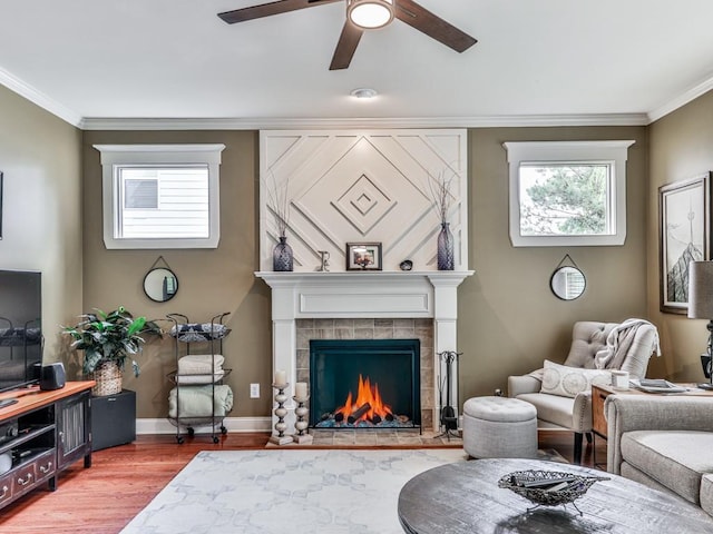 living area featuring wood finished floors, a ceiling fan, a fireplace, ornamental molding, and baseboards