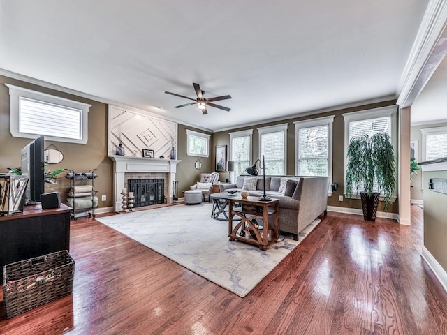 living room with a fireplace with flush hearth, crown molding, ceiling fan, wood finished floors, and baseboards
