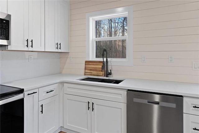 1337 Fairfield Dr, Lilburn, GA 30047 - kitchen with stainless steel appliances, wooden walls, white cabinetry, and light countertops