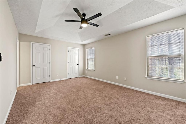 carpeted spare room featuring visible vents, baseboards, a ceiling fan, a raised ceiling, and a textured ceiling