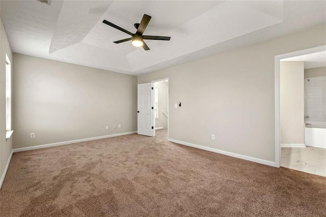 unfurnished bedroom with baseboards, a ceiling fan, ensuite bathroom, a tray ceiling, and carpet flooring